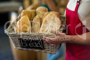 Mid section of male staff holding a basket of baguettes at counter