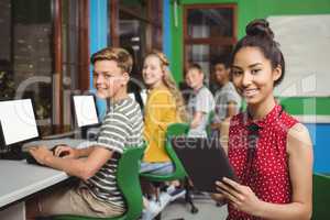 Smiling students studying on digital tablet and computer in classroom