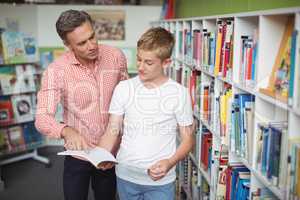 Teacher assisting student in reading book in library