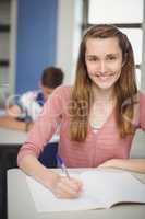 Portrait of smiling schoolgirl doing homework in classroom