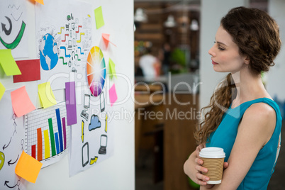 Thoughtful female executive looking at sticky notes on white wall