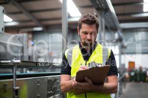 Factory worker writing on clipboard in factory