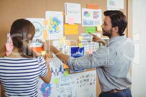 Male and female executives discussing over bulletin board