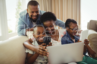 Parents and kids using laptop, smartphone and digital tablet on sofa