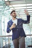 Businessman waving hand while having coffee at railway station