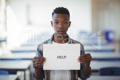 Schoolboy holding white paper with text sign in classroom