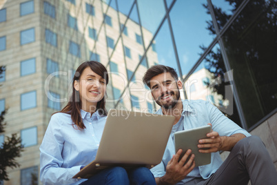 Executives using laptop and digital tablet outside office building