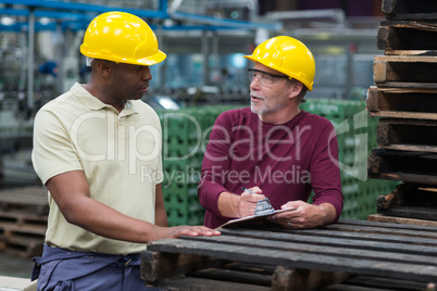 Factory workers discussing with a clipboard in drinks production plant