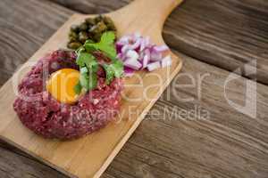 Minced meat with egg yolk, onions and olives on wooden tray