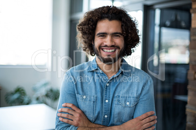 Smiling business executive standing with arms crossed in office