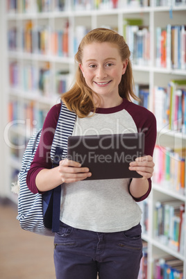 Portrait of happy schoolgirl holding digital tablet in library