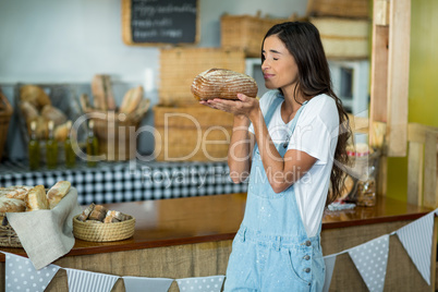 Smiling woman smelling a round loaf of bread at counter