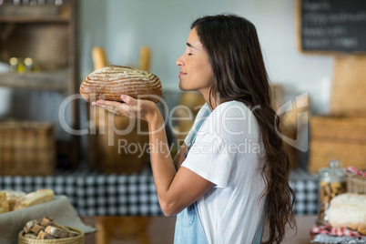 Smiling woman smelling a round loaf of bread at counter