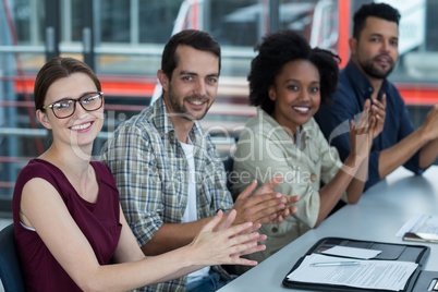 Smiling business executives clapping in meeting at office