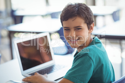 Portrait of schoolboy using laptop in classroom