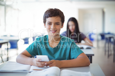 Portrait of schoolboy using mobile phone while studying in classroom
