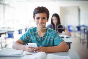 Portrait of schoolboy using mobile phone while studying in classroom
