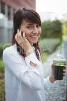 Executive talking on mobile phone while having juice on road