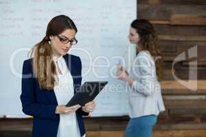 Businesswoman using digital tablet while colleague working in background