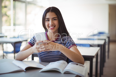 Portrait of schoolgirl using mobile phone while studying in classroom