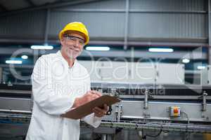 Smiling factory engineer maintaining record on clipboard in factory