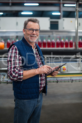 Smiling factory worker using digital tablet at drinks production plant