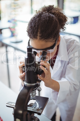 Attentive schoolgirl looking through microscope in laboratory