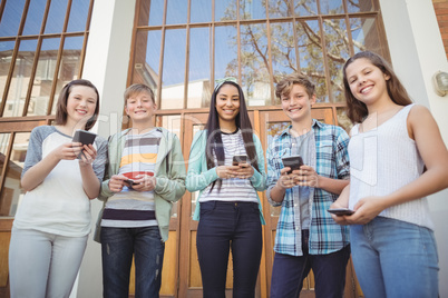 Portrait of smiling school friends using mobile phone in campus