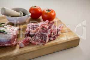 Rib chop, stone grinder and tomatoes on wooden board
