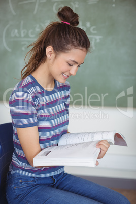 Schoolgirl sitting on chair and holding a book in classroom