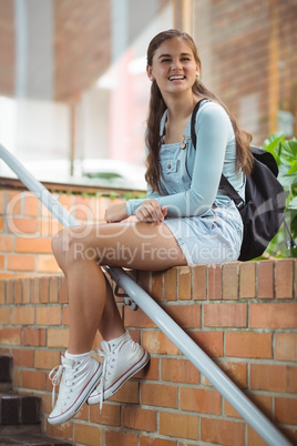 Happy schoolgirl sitting on brick wall
