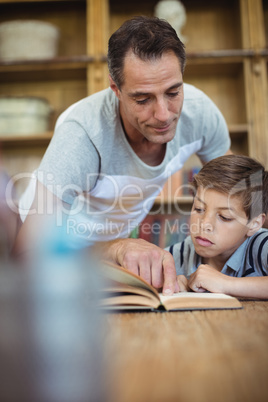 Father and son reading a book in study room