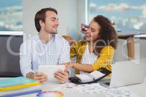 Smiling graphic designers sitting at table and using digital tablet