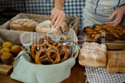 Mid section of female staff holding croissant with tong at counter