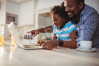 Father using laptop while assisting his daughter with homework