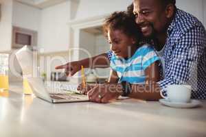 Father using laptop while assisting his daughter with homework