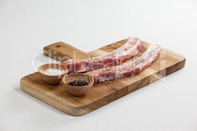 Sirloin chops, salt and black pepper on wooden board
