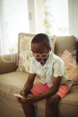 Boy sitting on sofa and using mobile phone in living room