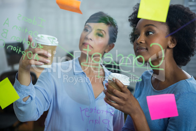 Female graphic designers with disposable cup reading text on the glass