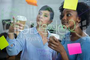 Female graphic designers with disposable cup reading text on the glass