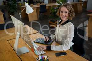 Female graphic designer smiling while using desktop pc and graphic tablet