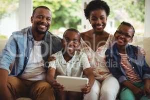 Parents and son using digital tablet on sofa in living room