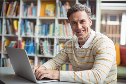 Portrait of happy school teacher using laptop in library