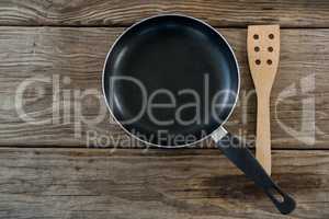 Pan and wooden spatula against wooden background