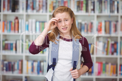 Portrait of sad schoolgirl standing with schoolbag in library