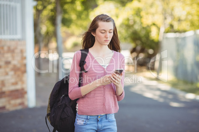School girl with schoolbag using mobile phone in campus