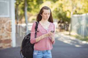School girl with schoolbag using mobile phone in campus