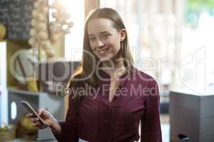 Portrait of smiling female staff using mobile phone at counter