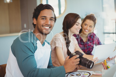Portrait of fashion designer holding digital camera with colleagues in background