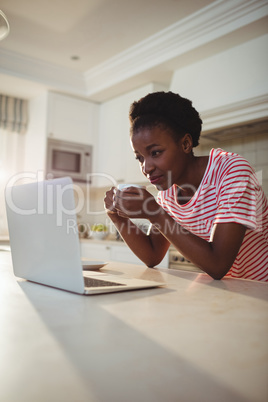 Woman using laptop while having coffee in kitchen